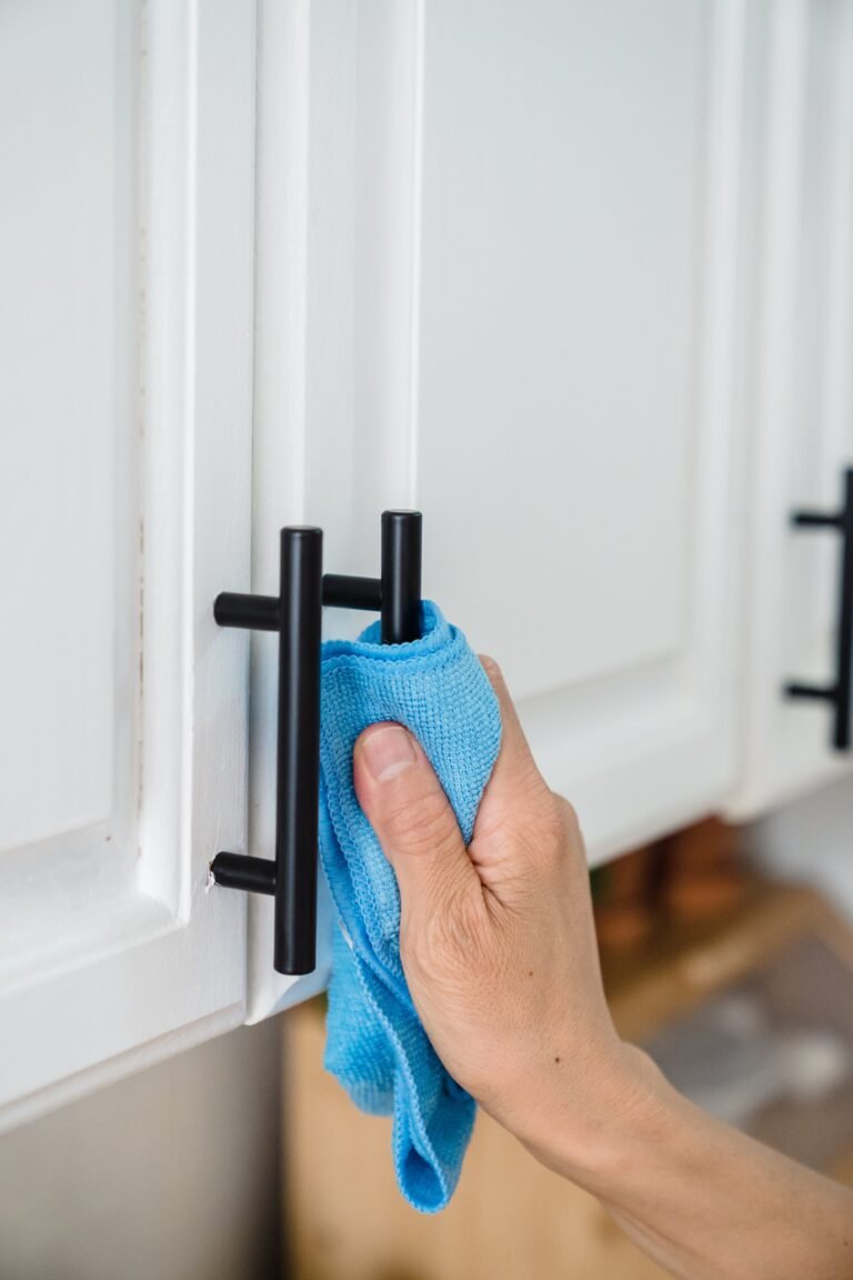 Hand wiping a black cabinet pull on a white cabinet door with a blue microfiber cloth