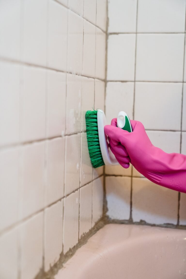 Gloved hand scrubbing tile grout with a stiff brush