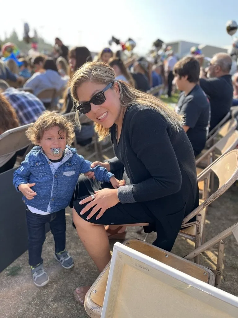 Lina crouching next to young Benji at an outdoor family event