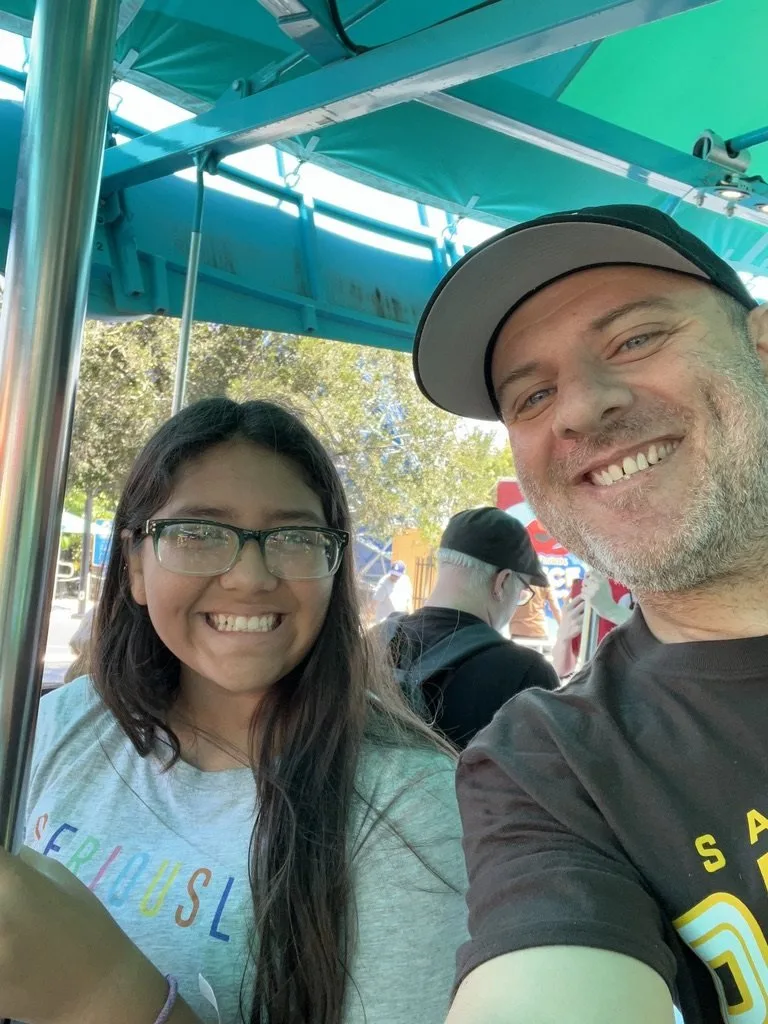 Paul and his daughter smiling for a selfie beneath a teal canopy at an outdoor event