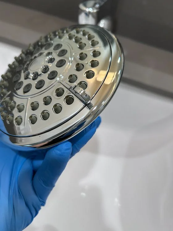 Close-up of a gloved hand cleaning a chrome showerhead and faucet during a detail cleaning