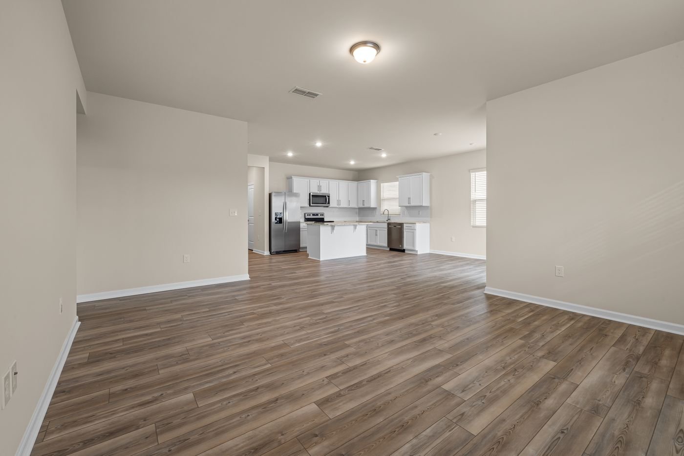 Empty room with plank floors and a view into the kitchen