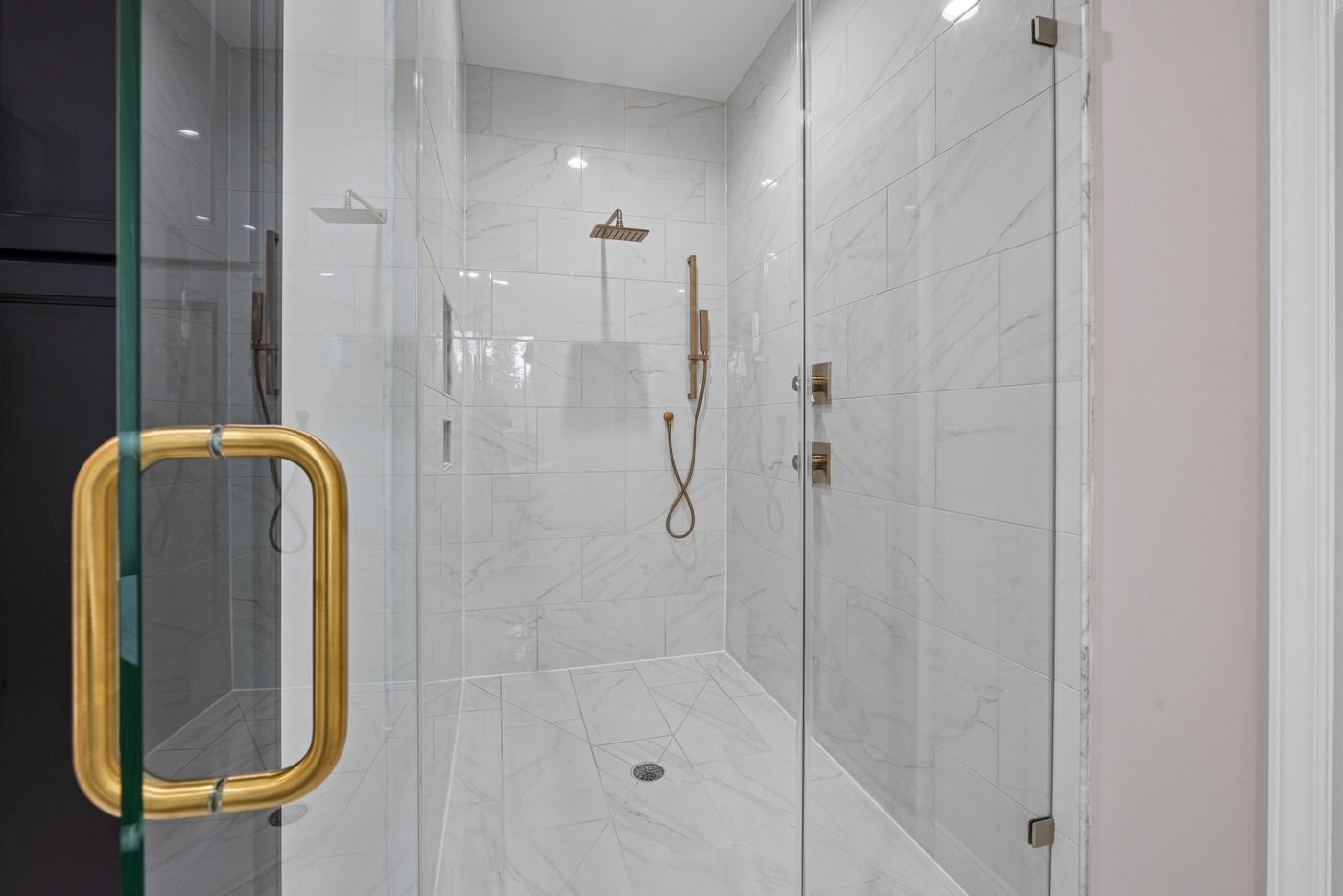 Frameless glass shower door with a brass handle and marble-look tile