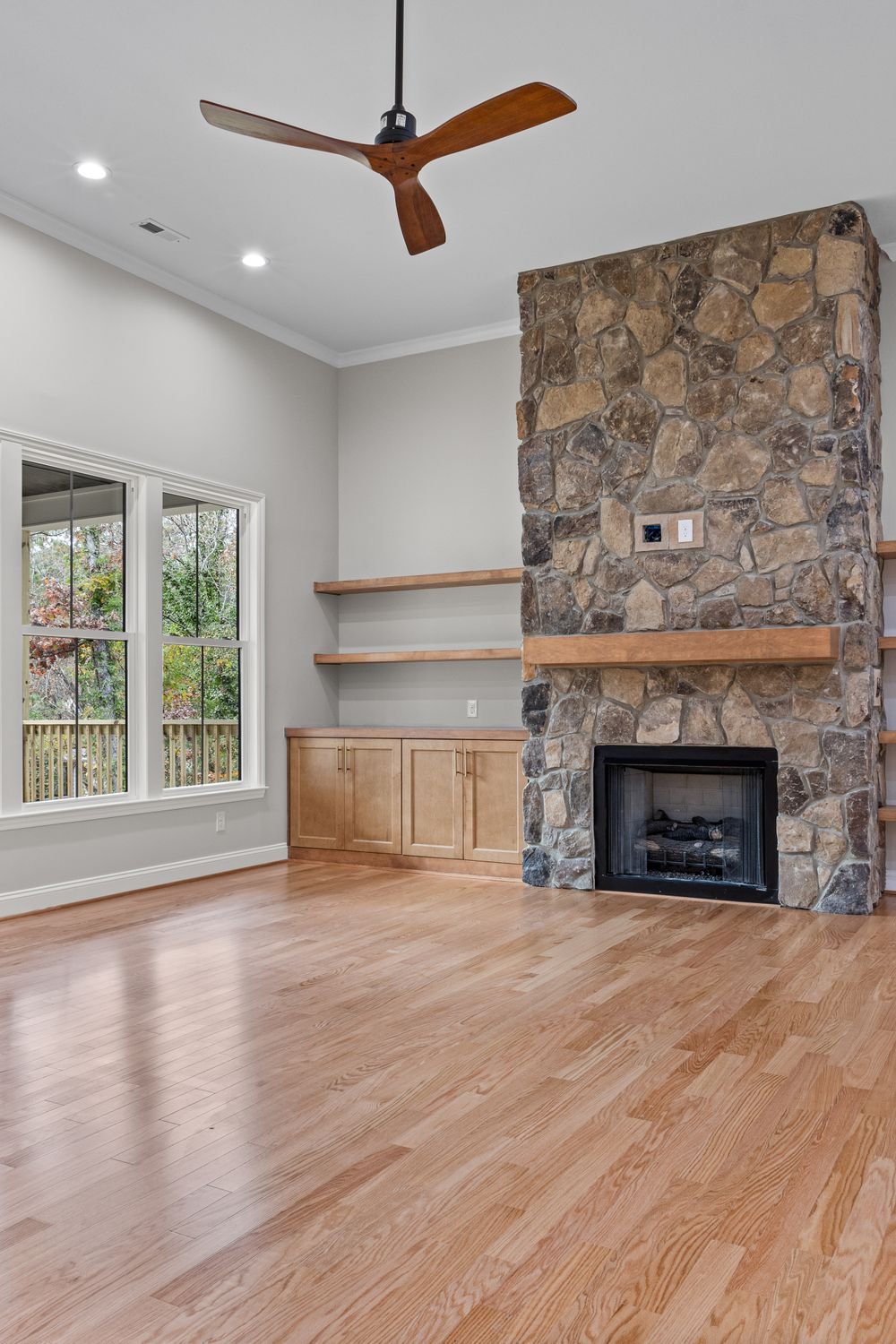 Living room with a ceiling fan, stone fireplace and hardwood floors