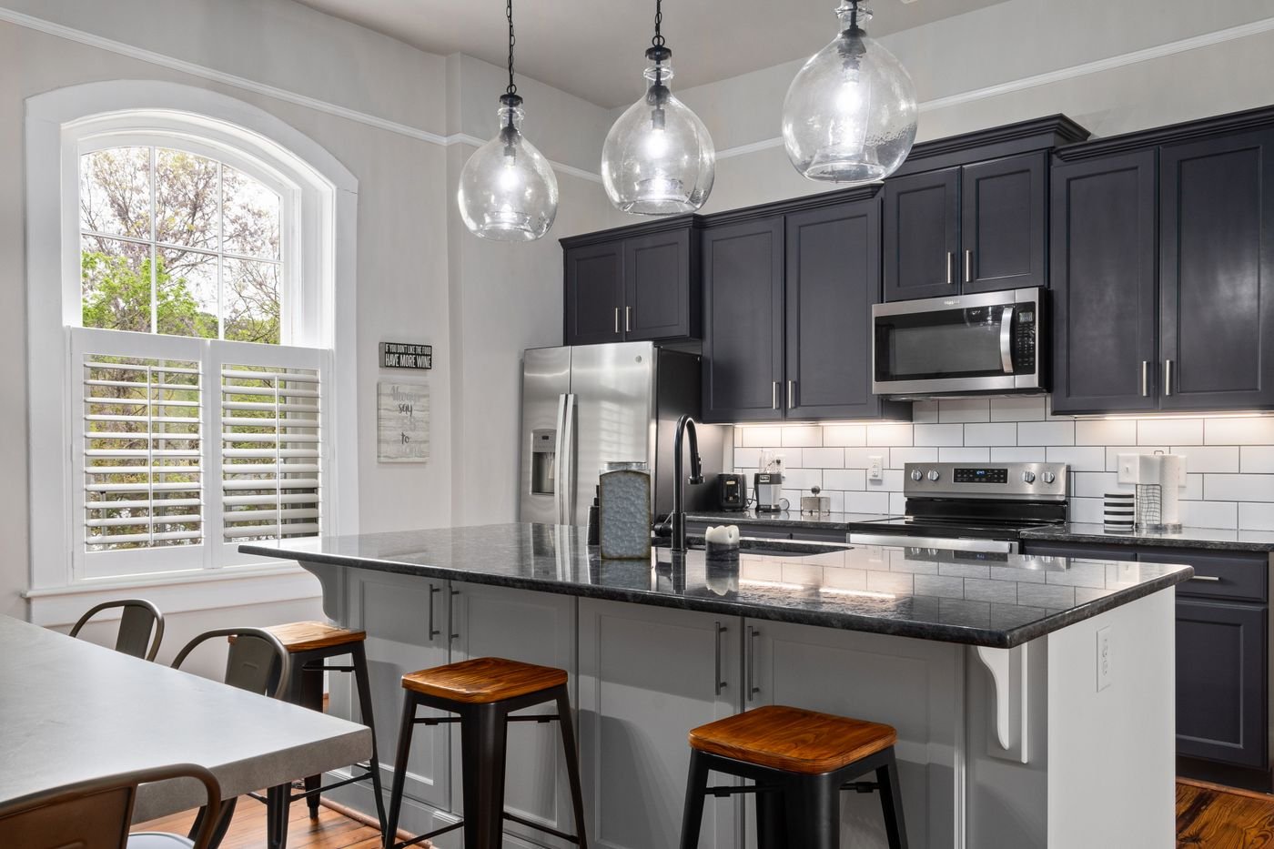 Kitchen with dark navy painted cabinets, a granite island and wooden bar stools