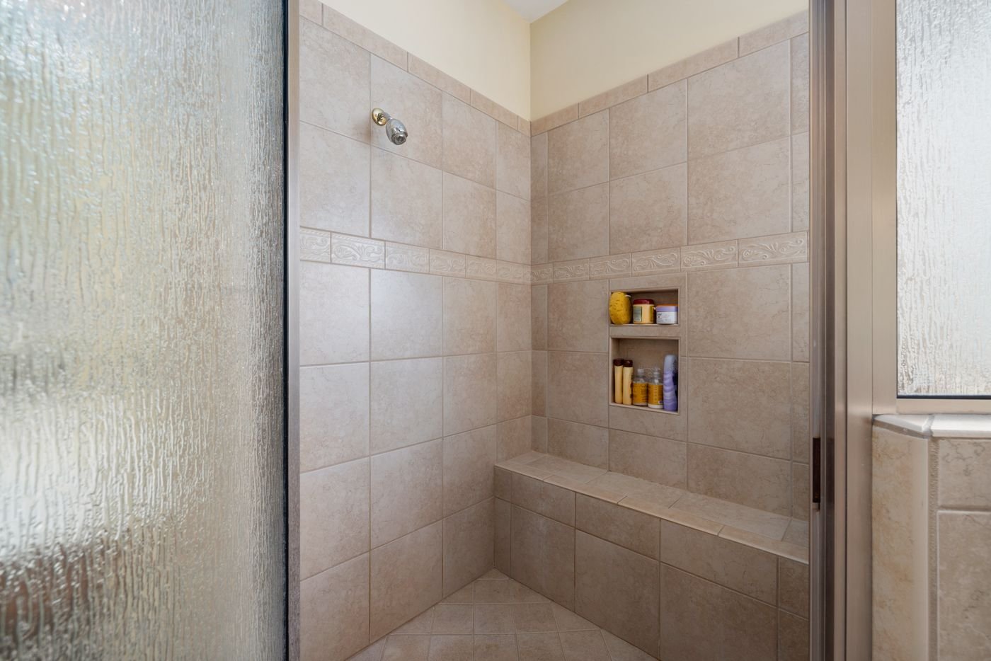 Walk-in tiled shower with a textured glass door and built-in bench