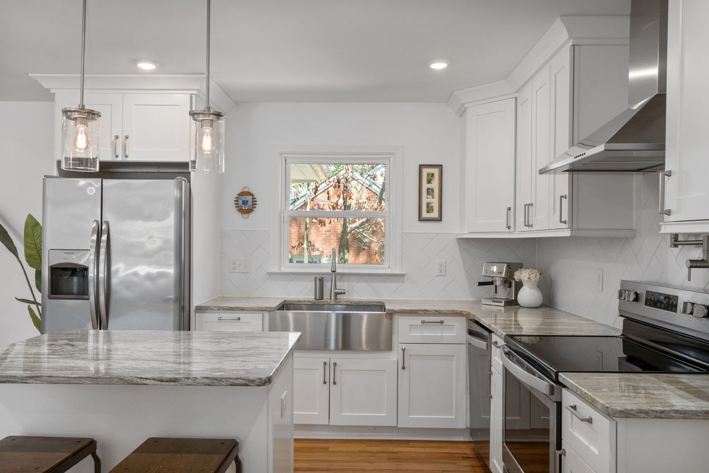 White kitchen with a range hood over the stove, farmhouse sink and window