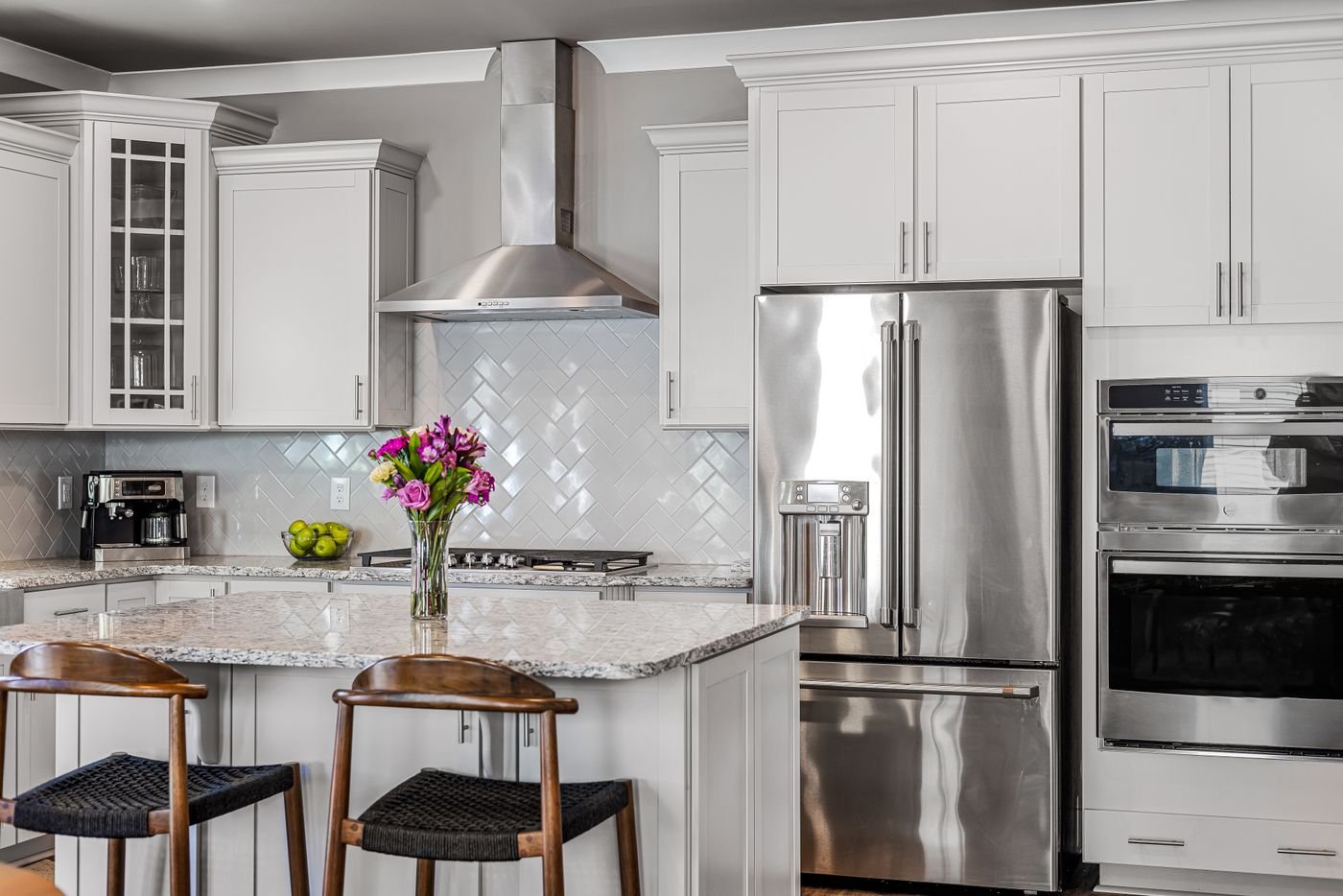 White kitchen with stainless range hood, wall ovens and refrigerator