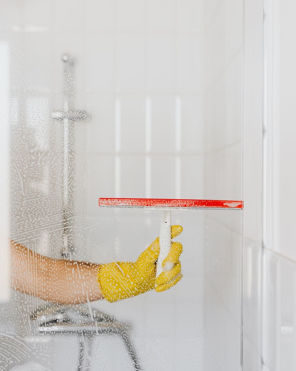 Gloved hand running a squeegee across a wet glass shower door
